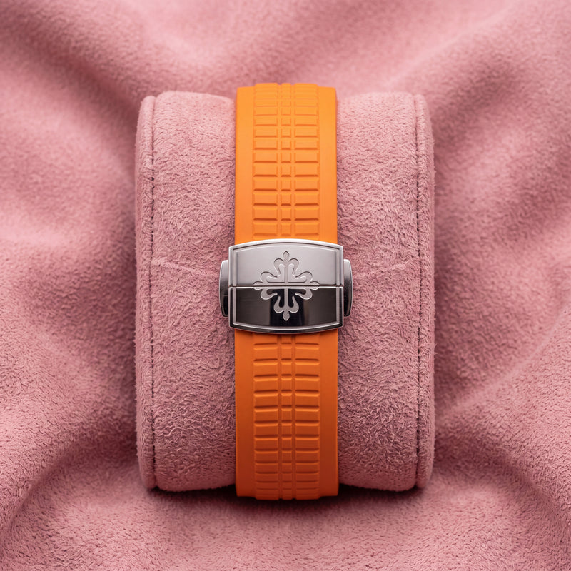 Orange textured Aquanaut strap with silver-toned cross-emblem clasp on a pink cushion