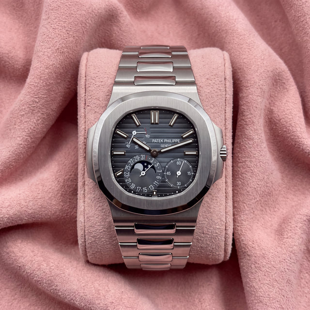 Patek Philippe Nautilus 5712/1A-001 with blue-grey striped moon-phase dial and integrated silver-toned bracelet on a pink cushion