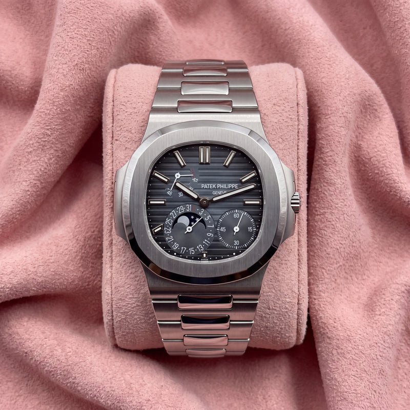 Patek Philippe Nautilus 5712/1A-001 with blue-grey striped moon-phase dial and integrated silver-toned bracelet on a pink cushion