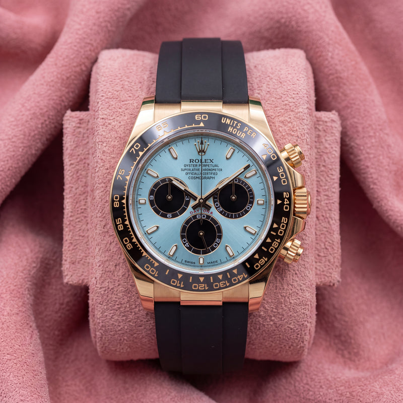 Front view of turquoise-blue dial Daytona with black chronograph registers, dark bezel and black strap on pink cushion