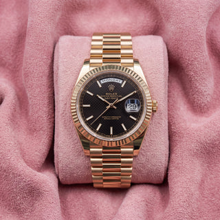 Rolex Day-Date 40 with black dial, fluted bezel and gold-tone President bracelet on a pink cushion