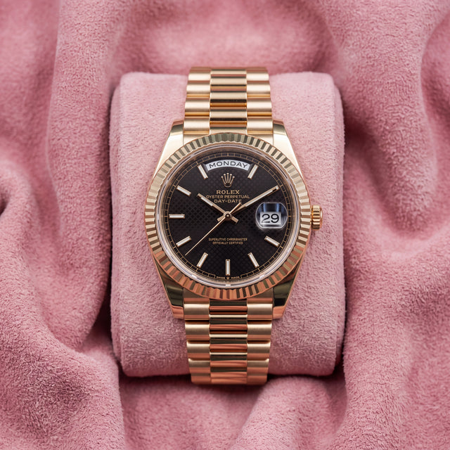 Rolex Day-Date 40 with black dial, fluted bezel and gold-tone President bracelet on a pink cushion
