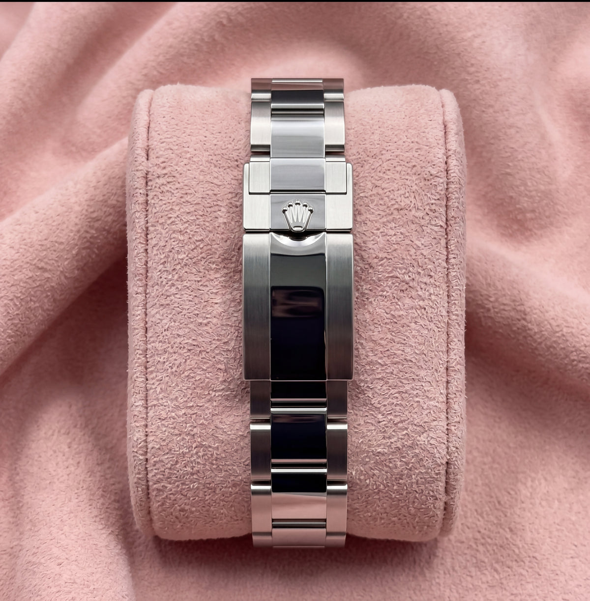 Steel watch bracelet and crown-emblem clasp shown from the rear on pink cushion