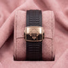 Dark brown textured Aquanaut strap with rose-toned cross-emblem clasp on a pink cushion