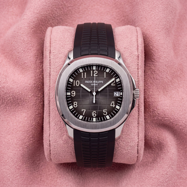 A Patek Philippe Nautilus watch with a black dial and black rubber strap, displayed on a pink velvet cushion.