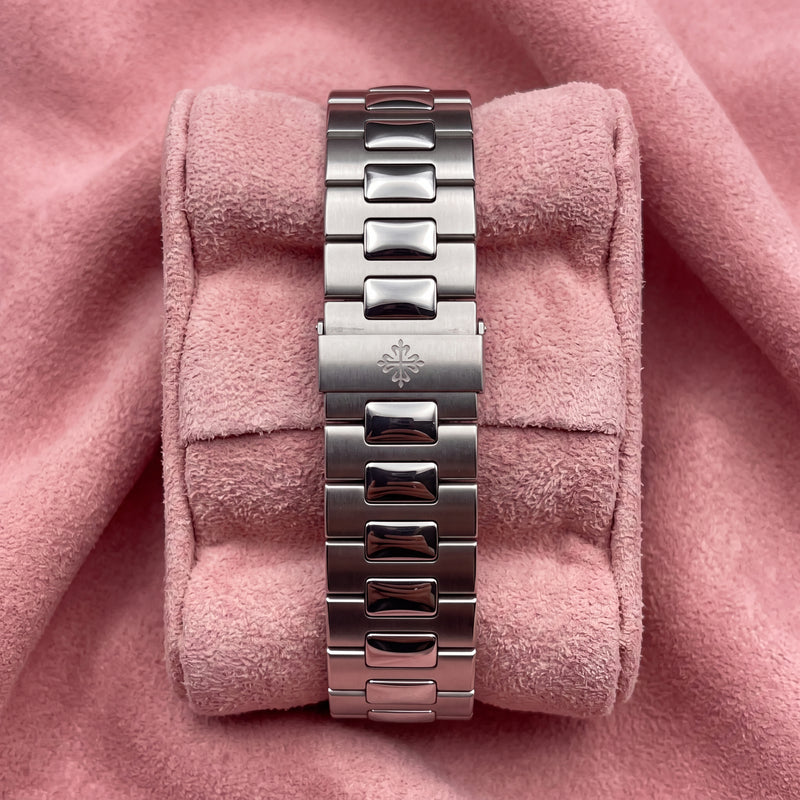 A silver stainless steel link watch band displayed on a pink velvet cushion, set against a matching pink fabric background.