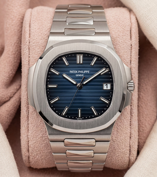 Blue-dial watch with rounded octagonal case and integrated metal bracelet on a pink cushion