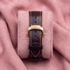 Brown leather strap with contrasting stitching and rose-toned Nautilus-engraved clasp on a pink cushion