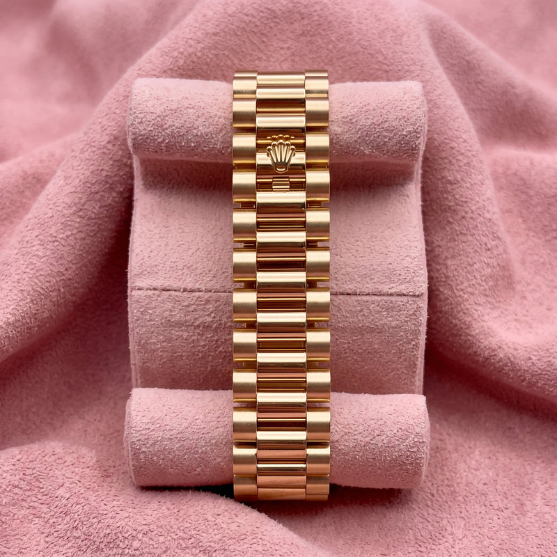 Gold-tone Rolex President bracelet with crown detail on a pink cushion