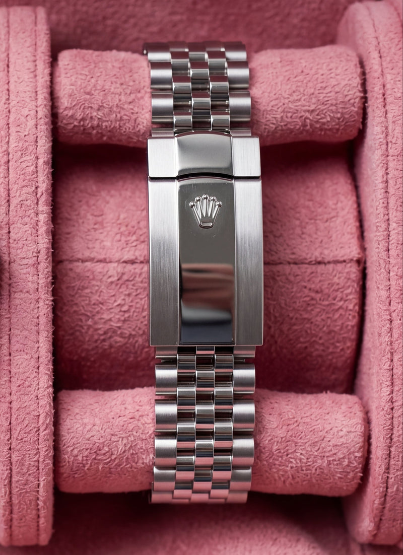 A Rolex Oyster Perpetual Datejust watch with a blue dial and stainless steel Oyster bracelet, displayed inside a pink velvet watch box alongside a matching bracelet clasp.