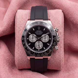 Front view of black-dial Daytona chronograph with dark tachymeter bezel and black strap on pink cushion