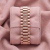 Rear view of rose-tone three-link watch bracelet with crown-emblem clasp on pink cushion