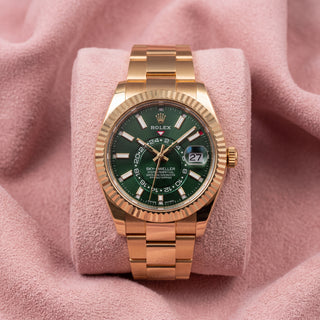 Rolex Sky-Dweller with green dial, gold-tone fluted bezel and Oyster bracelet on a pink cushion