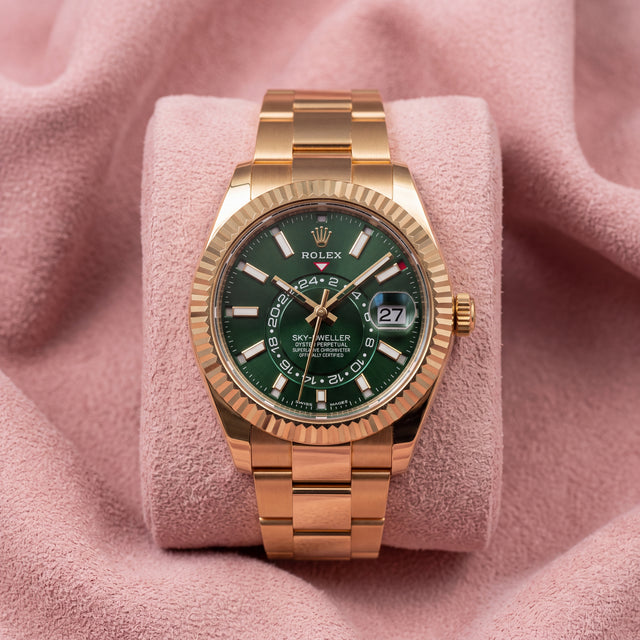 Rolex Sky-Dweller with green dial, gold-tone fluted bezel and Oyster bracelet on a pink cushion